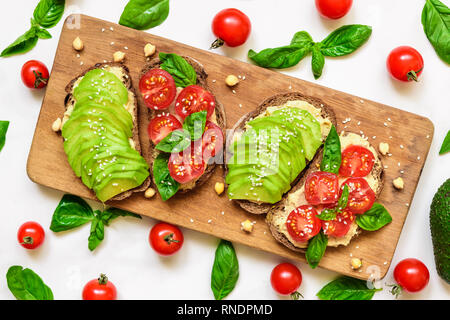 Toast à l'avocat. Toasts sain avec de l'avocat, les tomates cerises, le basilic et les graines de sésame sur planche à découper en bois. Vue de dessus Banque D'Images