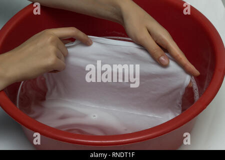 La jeune fille efface un T-shirt blanc dans un bassin rouge de stains, nettoie de stain remover, close-up, les mains, fond blanc, nettoyage Banque D'Images