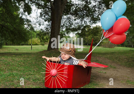 Cute toddler avec aviator hat pleurer dans un papier rouge avion fait main avec des ballons. Selective focus Banque D'Images