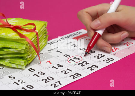 Une pile de coussins et une fille entoure les jours sur le calendrier avec un feutre rouge lorsqu'elle a ses menstruations, close-up, sur fond rose, gyneco Banque D'Images