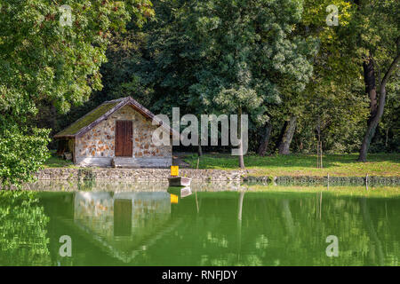 Confortable, coin pittoresque dans le parc. Une petite maison en pierre au bord du lac, un bateau sur l'eau et le reflet dans le lac. Au Nouveau-Brunswick, l'Europe, la Hongrie, t Banque D'Images