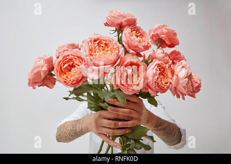 Young Girl's hands holding est un bouquet de fleurs fraîches dans ses mains avec tatoo dans une couleur de l'année 2019 Pantone Corail vivant Banque D'Images