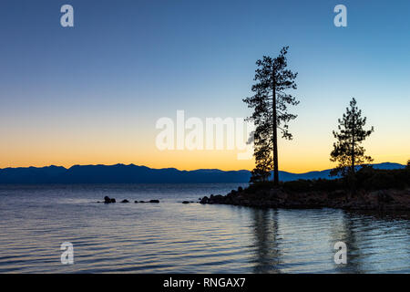 Ciel clair au coucher du soleil au port de sable avec l'eau calme, les silhouettes des arbres, et les montagnes en arrière-plan, le lac Tahoe, Carson City, Nevada Banque D'Images