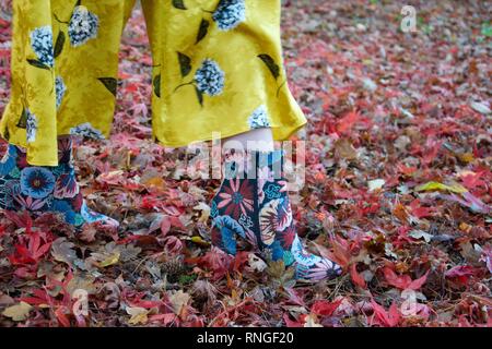 Gros plan d'une cheville brodé floral boot sur le pied d'une dame, avec un pantalon évasé patterened jaune. Elle est tombée à feuilles d'érable rouges dans un w Banque D'Images