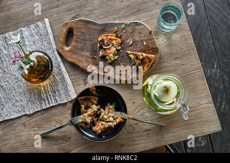 Des morceaux de pizza végétarienne dans un bol et sombre sur une planche en bois sur la table dans le café. Près de il y a un verre à limonade, verre, vase avec fleurs, Banque D'Images