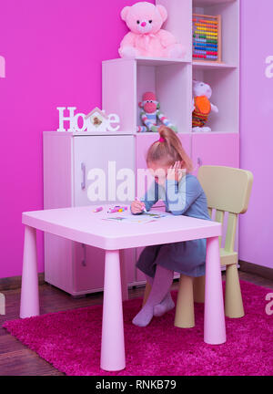 Jeune fille adorable de l'écriture, le dessin, l'apprentissage, assis, faire ses devoirs dans la chambre rose, de nombreux jouets sur étagère de meubles. Banque D'Images