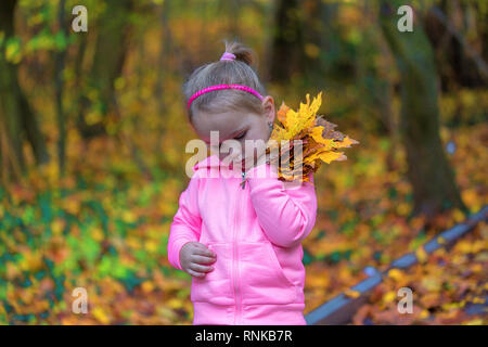 Peu triste girl holding feuilles tombées en automne parc. Les jeunes enfants douloureux détient des lames. Petit cœur brisé femelle en forêt sombre. Banque D'Images