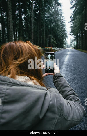 Smartphone dans la main sur la route d'arrière-plan dans les bois. Woman taking photo de la route. Banque D'Images