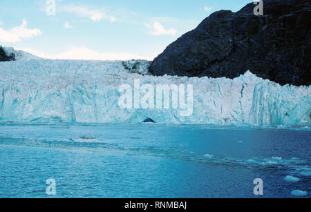 1980 - Le pont de ce navire à partir d'août 1980 Photo de Muir et glacier Muir Inlet, et la Réserve de parc national Glacier Bay, St. Elias, Alaska, montre les près de 200 pieds de hauteur de marée en retraite fin de Muir Glacier avec une partie de son visage couronné par quelques pinacles angulaires de glace, appelé séracs. Remarque l'icebergs dans le sillage du navire dans la partie inférieure droite de la photographie. Banque D'Images