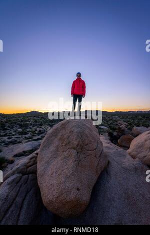 Jeune femme debout sur les rochers de granit ronds au coucher du soleil, des formations rocheuses, réservoir Blanc Camping, Joshua Tree National Park Banque D'Images