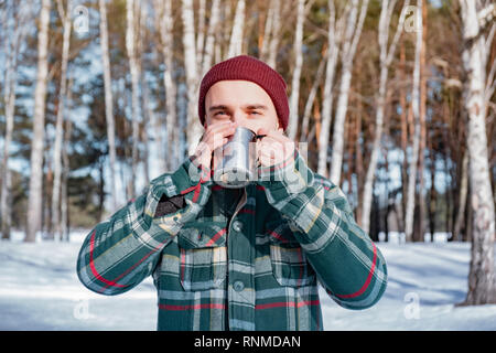 Personne de sexe masculin des boissons dans une tasse dans une forêt d'hiver enneigé. L'homme en chemise à carreaux est titulaire d'tasse de café en plein air Banque D'Images