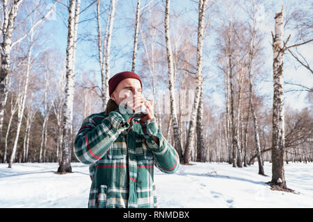 Personne de sexe masculin des boissons dans une tasse dans une forêt d'hiver enneigé. L'homme en chemise à carreaux est titulaire d'tasse de café en plein air et bénéficie d beau temps Banque D'Images