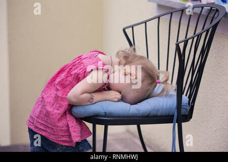 Petite fille boude et cachant son visage sur un coussin de chaise Banque D'Images