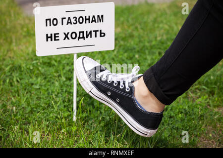 Les adolescents au pied sur l'herbe verte près de petite bannière blanche avec texte russe : Ne pas marcher sur la pelouse ! Banque D'Images