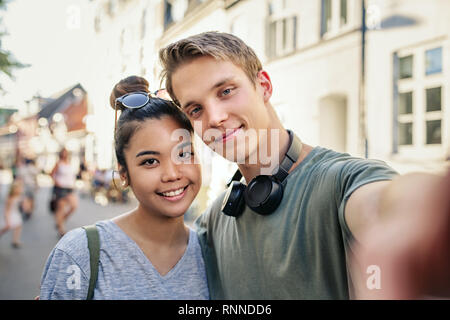Smiling young couple prenant un ensemble tout en selfies debout dans les bras dans une rue de la ville Banque D'Images