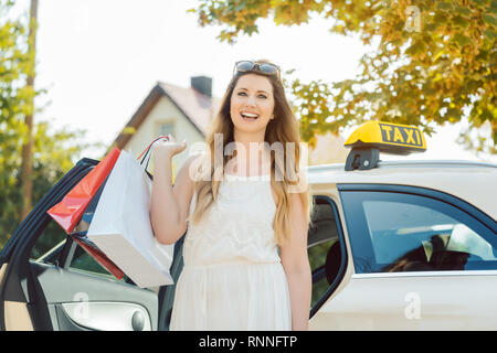 Femme sortir d'une voiture de taxi carrying shopping bags Banque D'Images