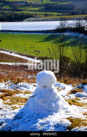 Un petit bonhomme avec des bâtons que les armes se trouve sur le bord des collines couvertes de neige du parc national des South Downs, East Sussex, UK, le village de G Banque D'Images