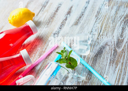 Les bouteilles en plastique avec des petits fruits, boisson rafraîchissante. dispersés des cubes de glace et de pailles à boire. sur l'arrière-plan d'une table en bois miteux. close up copie. Banque D'Images