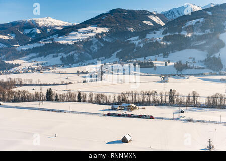 Le train rouge et blanc ÖBB passant le champs couverts de neige dans un paysage de montagne, d'hiver pittoresque massif du Dachstein, Liezen, Styrie, Autriche Banque D'Images