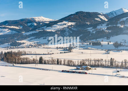 Le train rouge et blanc ÖBB passant le champs couverts de neige dans un paysage de montagne d'hiver pittoresque District, Liezen, Styrie, Autriche, Europe Banque D'Images