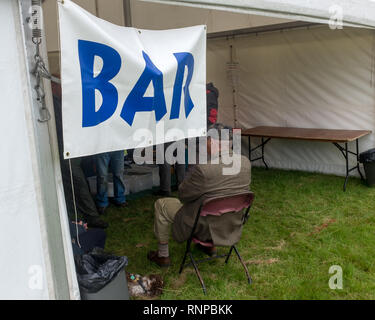 Un homme âgé assis à l'entrée de la tente à bière au salon de l'agriculture locale vu de derrière alors que les clients à l'intérieur des Highlands écossais, socalise Banque D'Images