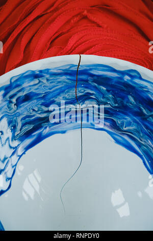 Close-up d'une fissure sur une plaque designer bleu et blanc sur fond rouge Banque D'Images