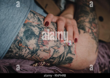 Gros plan d'une main de femme tendre avec red nails polish tenant un homme fort la main avec un manchon tattoo scarry. Banque D'Images