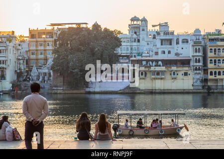 Certaines personnes s'asseoir et profiter du coucher du soleil à Udaipur tandis qu'un petit bateau de tourisme passe par dans le lac. Banque D'Images