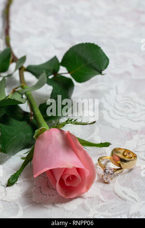 Rose rose avec large bande de mariage et bague de fiançailles en diamants sur un fond de dentelle blanche avec copie espace vertical Banque D'Images