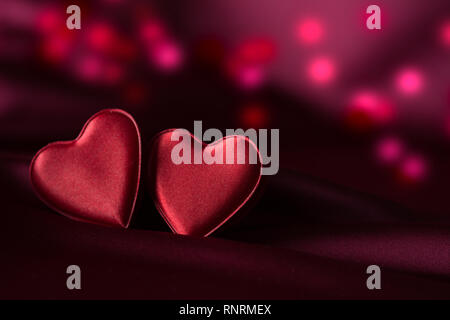 Deux coeurs rouges sur satin violet avec de délicats bokeh rouge et violet en arrière-plan Banque D'Images
