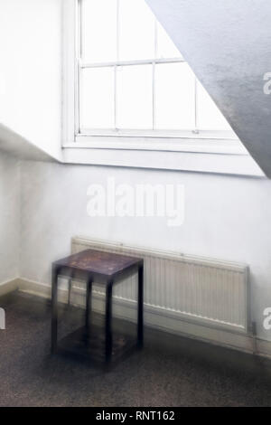 Zoom fantomatique image floue d'une fenêtre à guillotine lumineuses dans une sombre chambre d'une maison ancienne, avec une petite table en bois et le radiateur Banque D'Images