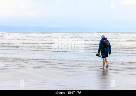 Homme seul marche pieds nus dans l'eau peu profonde sur la plage à Westward Ho !, Devon, UK, sur un matin d'été pluvieux et brumeux Banque D'Images