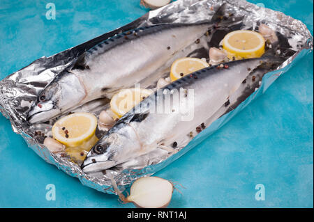 Le maquereau poisson avec les ingrédients pour la cuisson dans la feuille d'aluminium sur un fond bleu. D'aluminium est un produit domestique courante. Banque D'Images