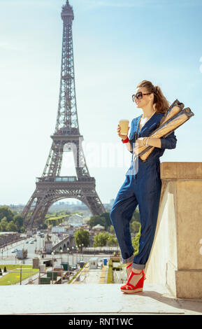 Voyageur moderne smiling woman in blue jeans avec l'ensemble tasse à café et deux baguettes aller à des attractions à Paris, France. Banque D'Images