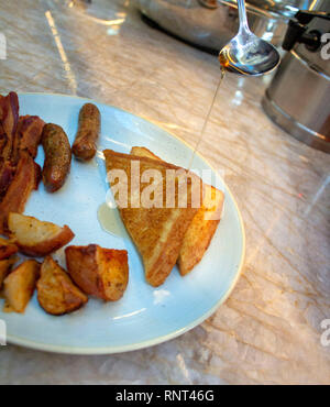 On verse le sirop sur du pain grillé sur une plaque avec du bacon, des saucisses et des pommes de terre. Banque D'Images