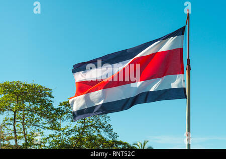 Le drapeau de la République démocratique du Costa Rica en Amérique centrale dans le vent avec des arbres en arrière-plan. Banque D'Images