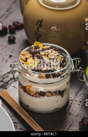 Photo verticale de yaourt blanc. Le yaourt est en petit pot de verre avec métal serrure et couvercle hermétique. Muesli avec des aliments secs est stratifié dans et sur le yogourt. Gla Banque D'Images