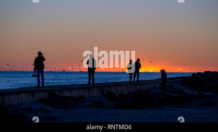 Un groupe de personnes sur la jetée sud à Port Aransas, Texas stand silhouetté contre le ciel juste avant le lever du soleil. Banque D'Images