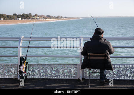 La pêche au large de l'homme d'une jetée victorienne anglais assis sur un tabouret avec des cannes à pêche sur le parapet en Carême Banque D'Images