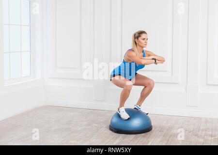 Portrait de sportif de concentration très belle jeune femme blonde athlétique en short noir et bleu top travaillant dans ce sport en exersice bosu balance trai