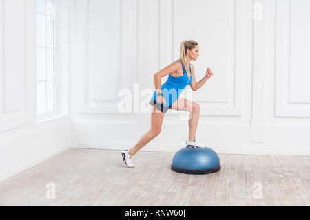 Vue de côté portrait de jeune sportif ciblé athletic blonde woman in black short et haut bleu travaillant dans ce sport en exersice BOSU Balance Trainer, m