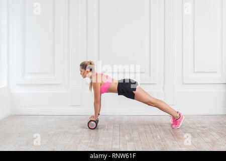 Vue côté profil portrait de jeune femme blonde athlétique en fit porter à l'aide de rouleau en mousse dans une salle de sport à la séance d'entraînement au poids de perte et faire plank. Rehabilitati Banque D'Images