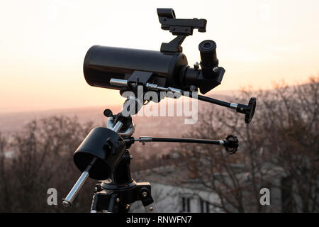 Un télescope monté sur un trépied, à la recherche, dans le cadre d'une grande ville au coucher du soleil Banque D'Images