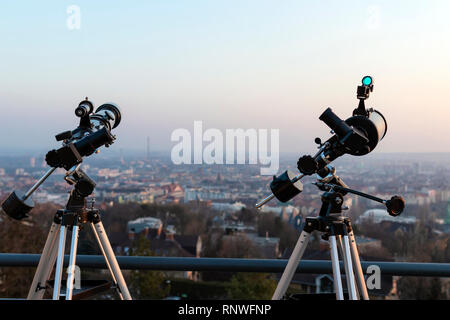 Deux télescopes professionnels, un télescope Newton et un réfracteur, montés sur trépieds sur une terrasse sur le toit, à la recherche, dans le cadre d'une grande ville au coucher du soleil. Banque D'Images