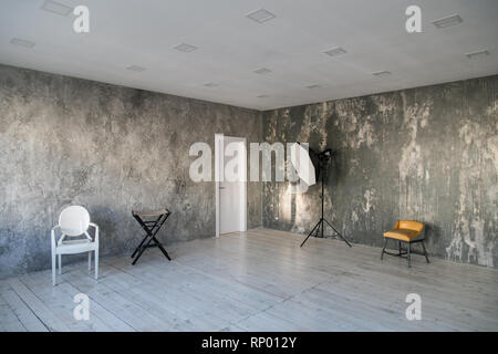 Lumière moderne de style loft avec des chaises de créateur et d'éclairage. Les murs gris avec la texture du béton. Plancher en bois. Banque D'Images