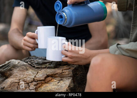 Femme versant de l'eau dans la tasse alors qu'il était assis avec l'homme dans l'aménagement forestier Banque D'Images