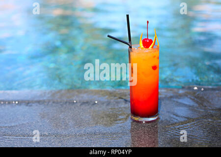 Avec un brillant verre Tequila Sunrise cocktail au bord de la piscine. On tropical Island resort de luxe Banque D'Images