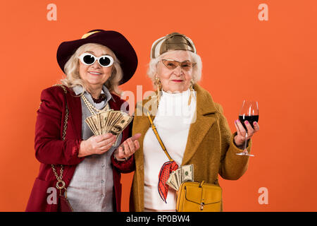 Cheerful senior woman holding argent près de ami avec verre de vin dans la main isolé sur orange Banque D'Images