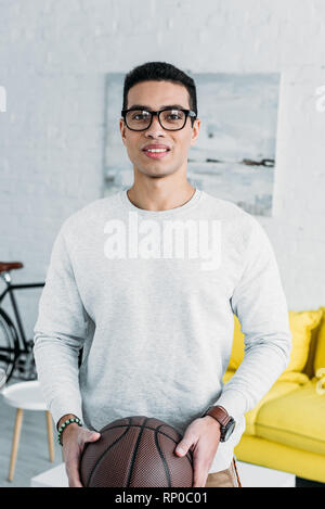 Handsome mixed race man en sweat et verres holding brown ball Banque D'Images