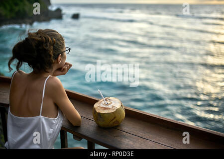 Femme dans les verres à la mer au coucher du soleil dans le café en plein air Banque D'Images